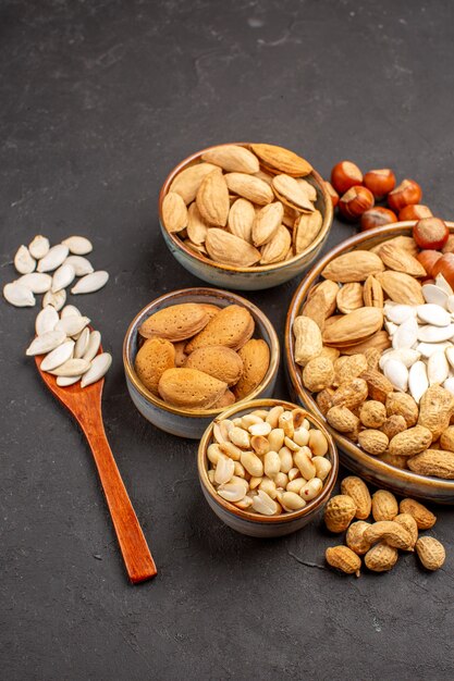 Vista frontal de diferentes nueces nueces frescas dentro de macetas en superficie oscura