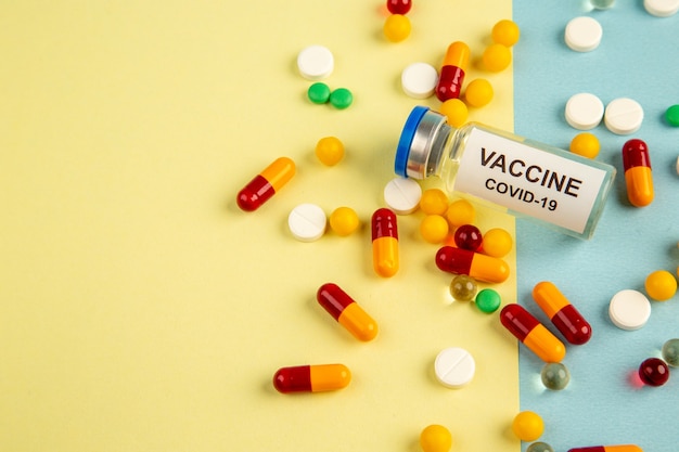 Vista frontal diferentes píldoras con vacuna sobre fondo amarillo-azul hospital pandémico covid- laboratorio de virus de ciencia drogas color de salud
