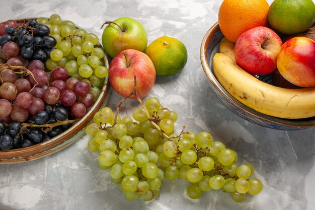 Vista frontal de diferentes uvas con otras frutas en la superficie blanca frutas verano jugo suave fresco