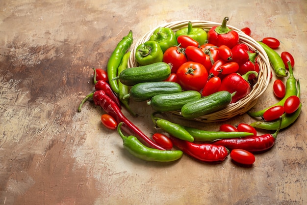 Vista frontal de diferentes verduras en una canasta de mimbre rodeada de pimientos y tomates cherry sobre fondo ámbar