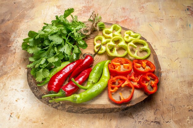 Vista frontal de diferentes verduras cilantro pimientos picantes pimientos cortados en trozos en un tablero de madera de árbol redondo sobre fondo ámbar