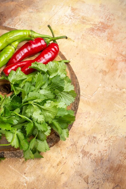 Vista frontal de diferentes verduras cilantro pimientos picantes en tablero de madera de árbol redondo en espacio libre de ámbar