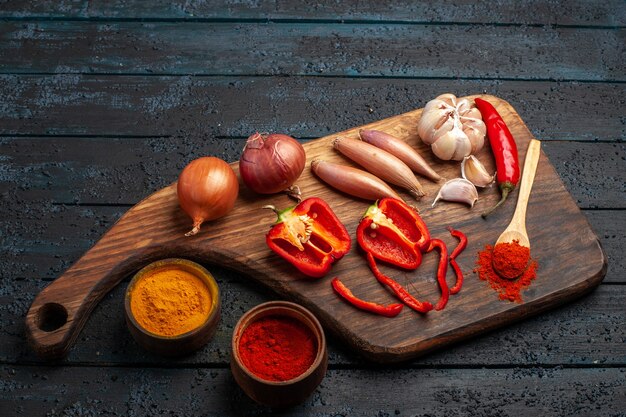 Vista frontal de diferentes verduras con condimentos en el escritorio oscuro