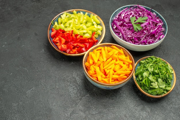 Vista frontal de diferentes verduras en rodajas con verduras en la mesa oscura