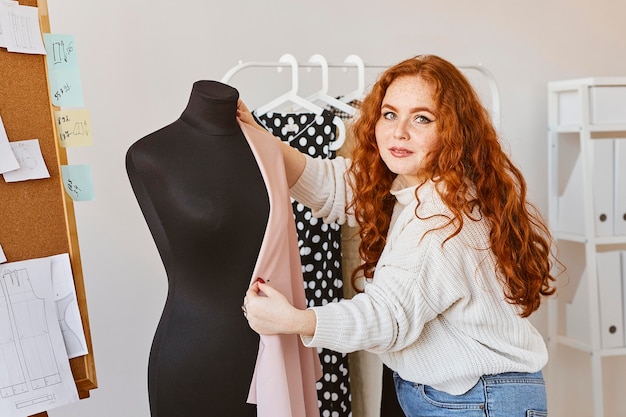 Vista frontal de la diseñadora de moda femenina que trabaja en un taller con forma de vestido