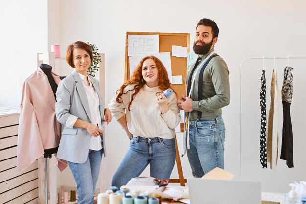 Vista frontal de diseñadores de moda sonrientes posando en su taller de negocios