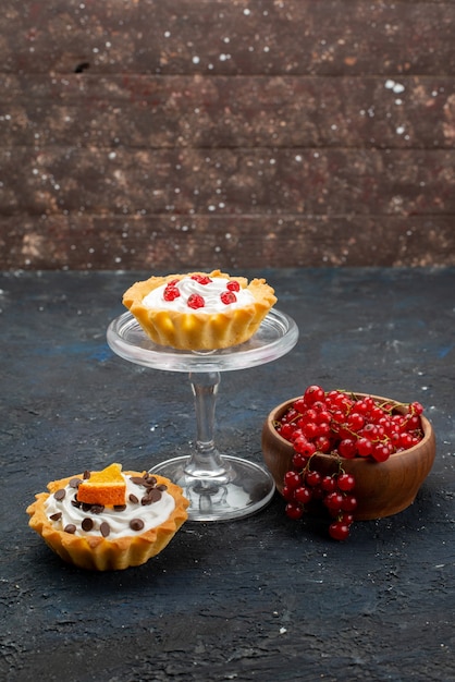 Foto gratuita vista frontal distante deliciosos pasteles con crema y frutas en la superficie oscura de la baya dulce