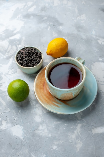 Foto gratuita vista frontal distante taza de té con limones frescos y té seco en la mesa de luz, color cítrico de frutas de té