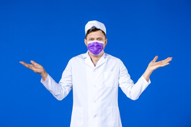 Vista frontal del doctor masculino sonriente en traje médico y máscara púrpura sobre azul