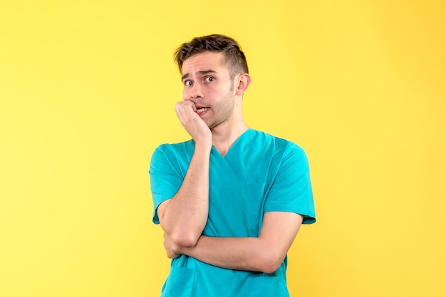 Vista frontal del doctor de sexo masculino que se siente nervioso en la pared amarilla