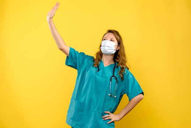 Vista frontal de la doctora agitando en máscara en la pared amarilla