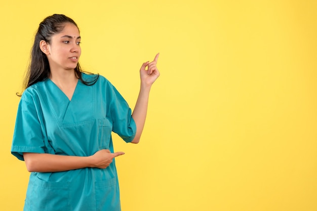 Vista frontal de la doctora bastante apuntando a algo en la pared amarilla