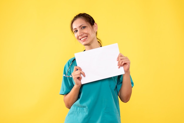 Vista frontal doctora en camisa médica con análisis de papel sobre fondo amarillo