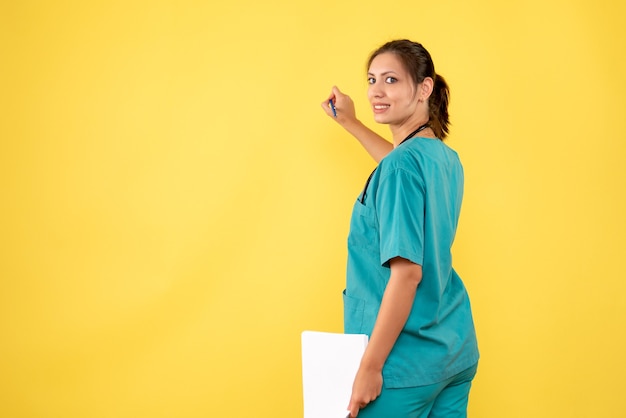 Vista frontal doctora en camisa médica con análisis de papel sobre fondo amarillo