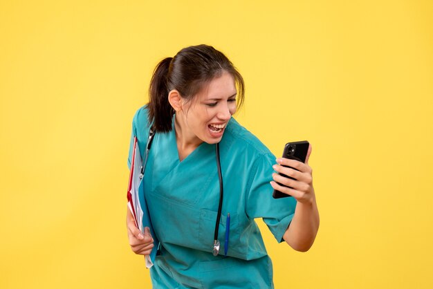 Vista frontal doctora en camisa médica con análisis y teléfono sobre fondo amarillo