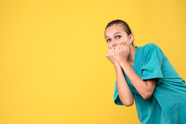 Vista frontal de la doctora en camisa médica con cara de miedo en la pared amarilla