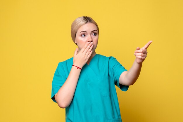 Vista frontal de la doctora en camisa médica con cara de sorpresa en la pared amarilla