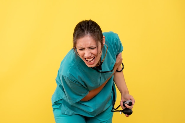 Vista frontal doctora en camisa médica comprobando su presión sobre fondo amarillo