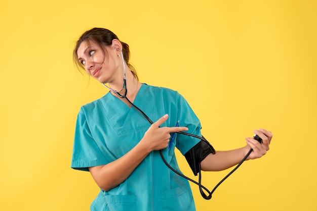 Vista frontal doctora en camisa médica comprobando su presión sobre fondo amarillo