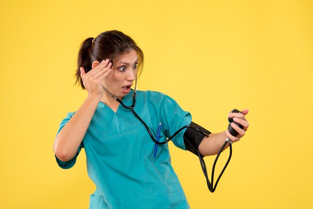 Vista frontal doctora en camisa médica comprobando su presión sobre fondo amarillo