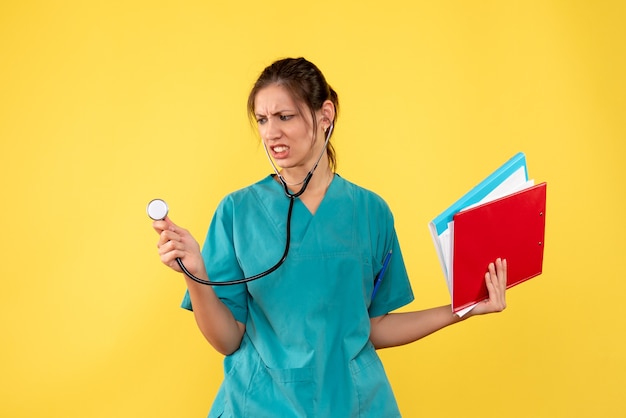 Vista frontal doctora en camisa médica con estetoscopio y notas sobre fondo amarillo