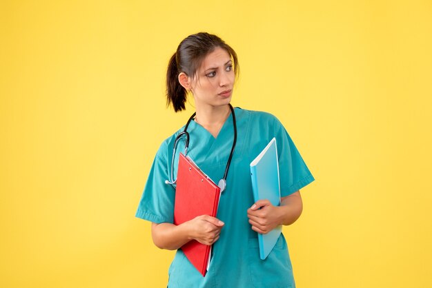 Vista frontal doctora en camisa médica con estetoscopio y notas sobre fondo amarillo