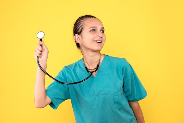 Vista frontal de la doctora en camisa médica con estetoscopio en pared amarilla