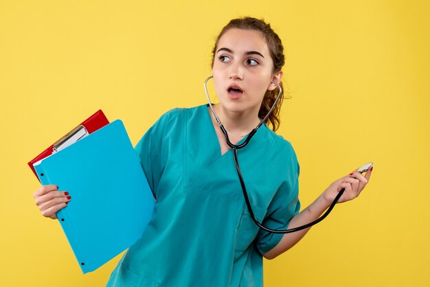 Vista frontal de la doctora en camisa médica con estetoscopio en pared amarilla