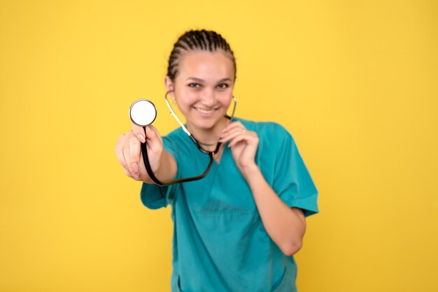 Vista frontal de la doctora en camisa médica con estetoscopio en pared amarilla