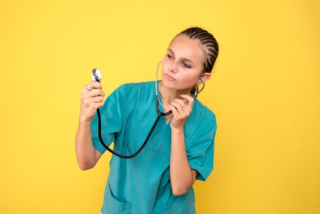 Vista frontal de la doctora en camisa médica con estetoscopio en pared amarilla