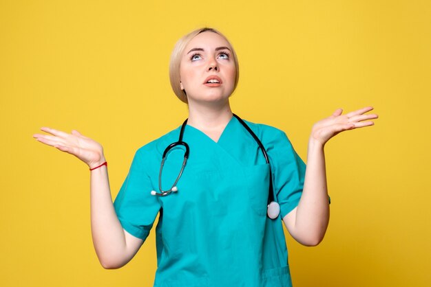 Vista frontal de la doctora en camisa médica con estetoscopio en pared amarilla