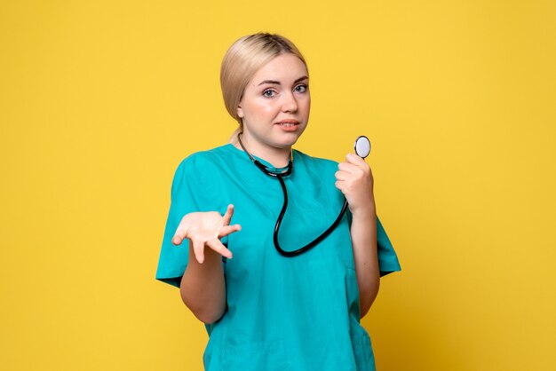 Vista frontal de la doctora en camisa médica con estetoscopio en pared amarilla