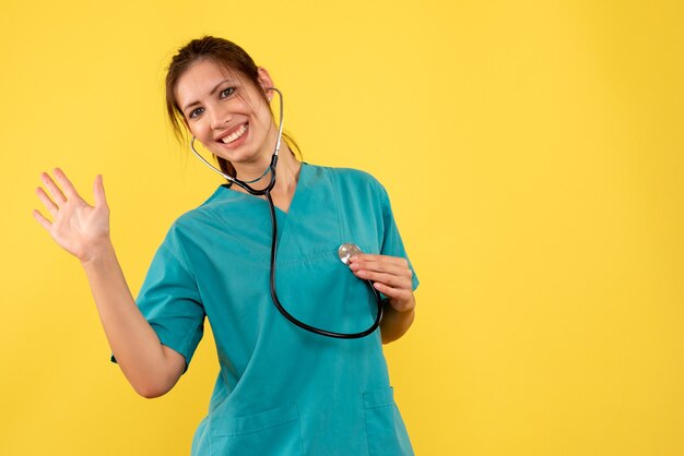 Vista frontal doctora en camisa médica con estetoscopio sobre fondo amarillo