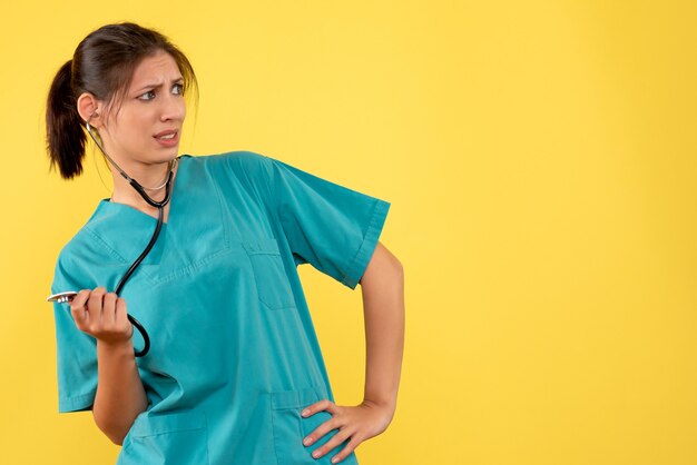 Vista frontal doctora en camisa médica con estetoscopio sobre fondo amarillo