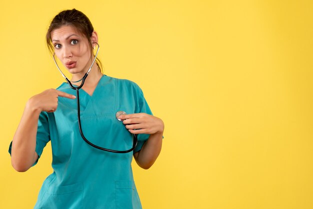 Vista frontal doctora en camisa médica con estetoscopio sobre fondo amarillo