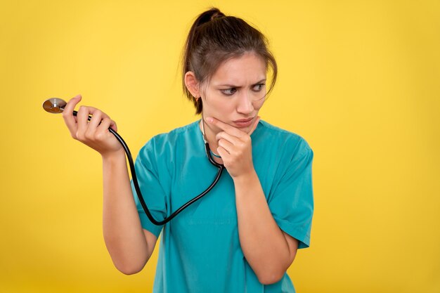 Vista frontal doctora en camisa médica con estetoscopio sobre fondo amarillo