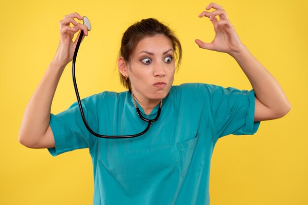 Vista frontal doctora en camisa médica con estetoscopio sobre fondo amarillo