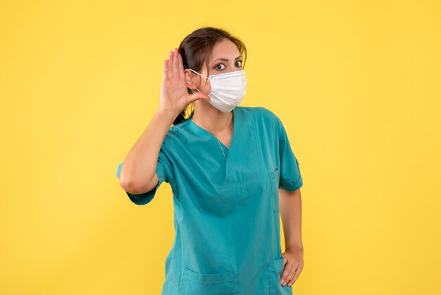 Vista frontal de la doctora en camisa médica y máscara estéril sobre fondo amarillo