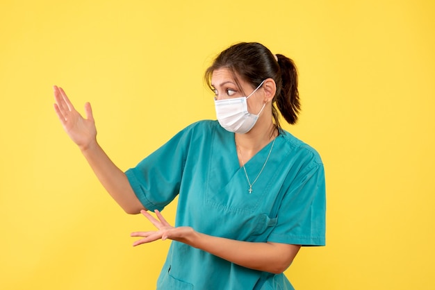 Vista frontal de la doctora en camisa médica y máscara estéril sobre fondo amarillo