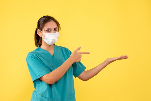 Vista frontal doctora en camisa médica y con máscara estéril sobre fondo amarillo