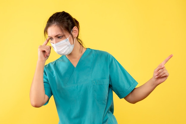 Vista frontal doctora en camisa médica y con máscara estéril sobre fondo amarillo