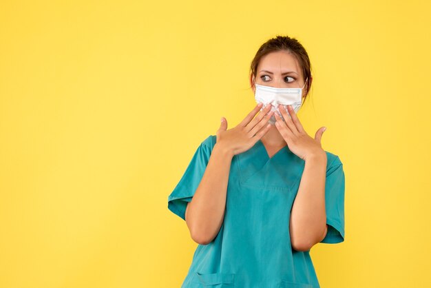 Vista frontal doctora en camisa médica y con máscara estéril sobre fondo amarillo