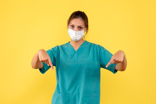 Vista frontal doctora en camisa médica y con máscara estéril sobre fondo amarillo