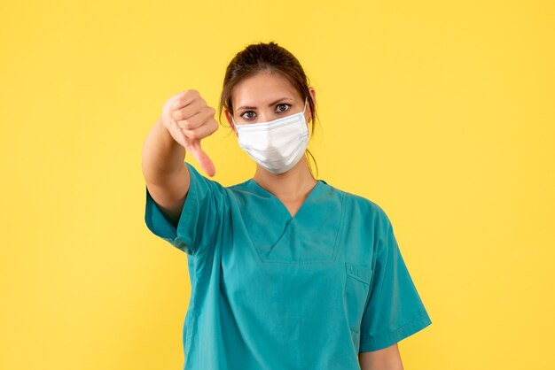 Vista frontal doctora en camisa médica y con máscara estéril sobre fondo amarillo