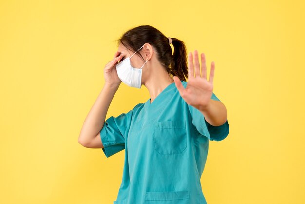 Vista frontal doctora en camisa médica y con máscara estéril sobre fondo amarillo