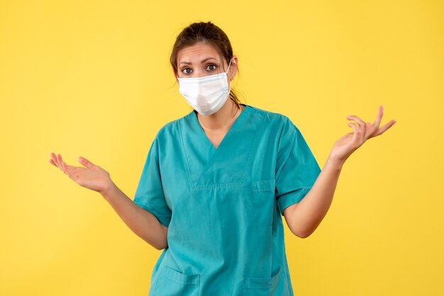 Vista frontal doctora en camisa médica y con máscara estéril sobre fondo amarillo