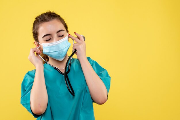 Vista frontal doctora en camisa médica y máscara con estetoscopio, color de virus emoción covid-19 salud