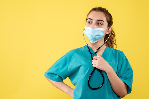 Vista frontal doctora en camisa médica y máscara con estetoscopio, virus color uniforme emoción covid-19 salud