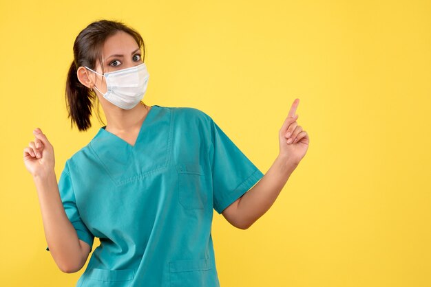 Vista frontal doctora en camisa médica y máscara sobre fondo amarillo