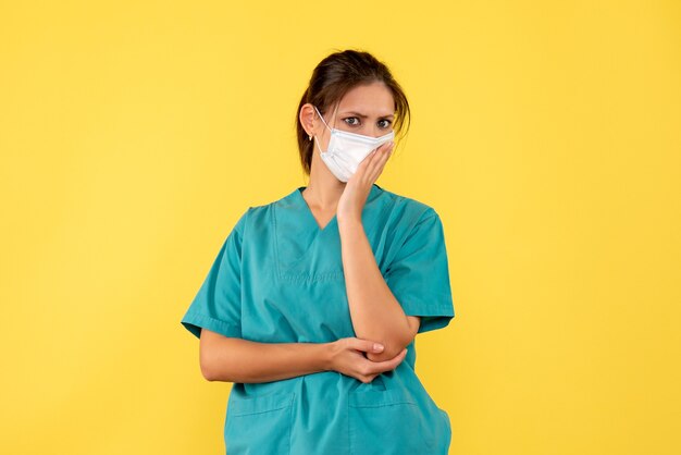 Vista frontal doctora en camisa médica y máscara sobre fondo amarillo